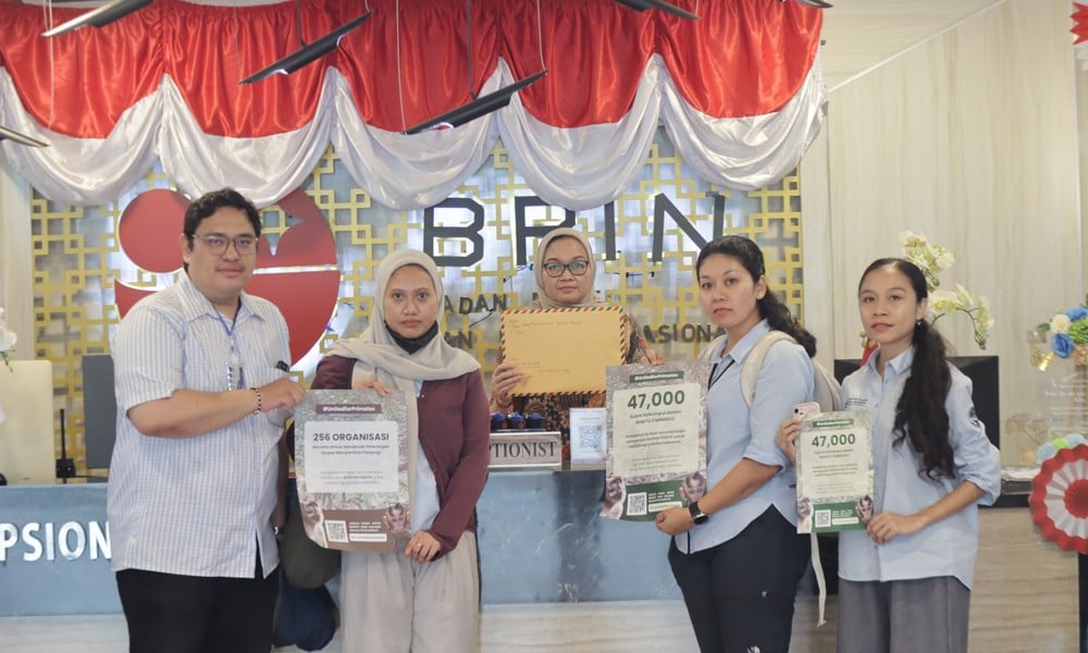 Five people hold petition materials in front of the BRIN sign at Indonesia's National Research and Innovation Agency.